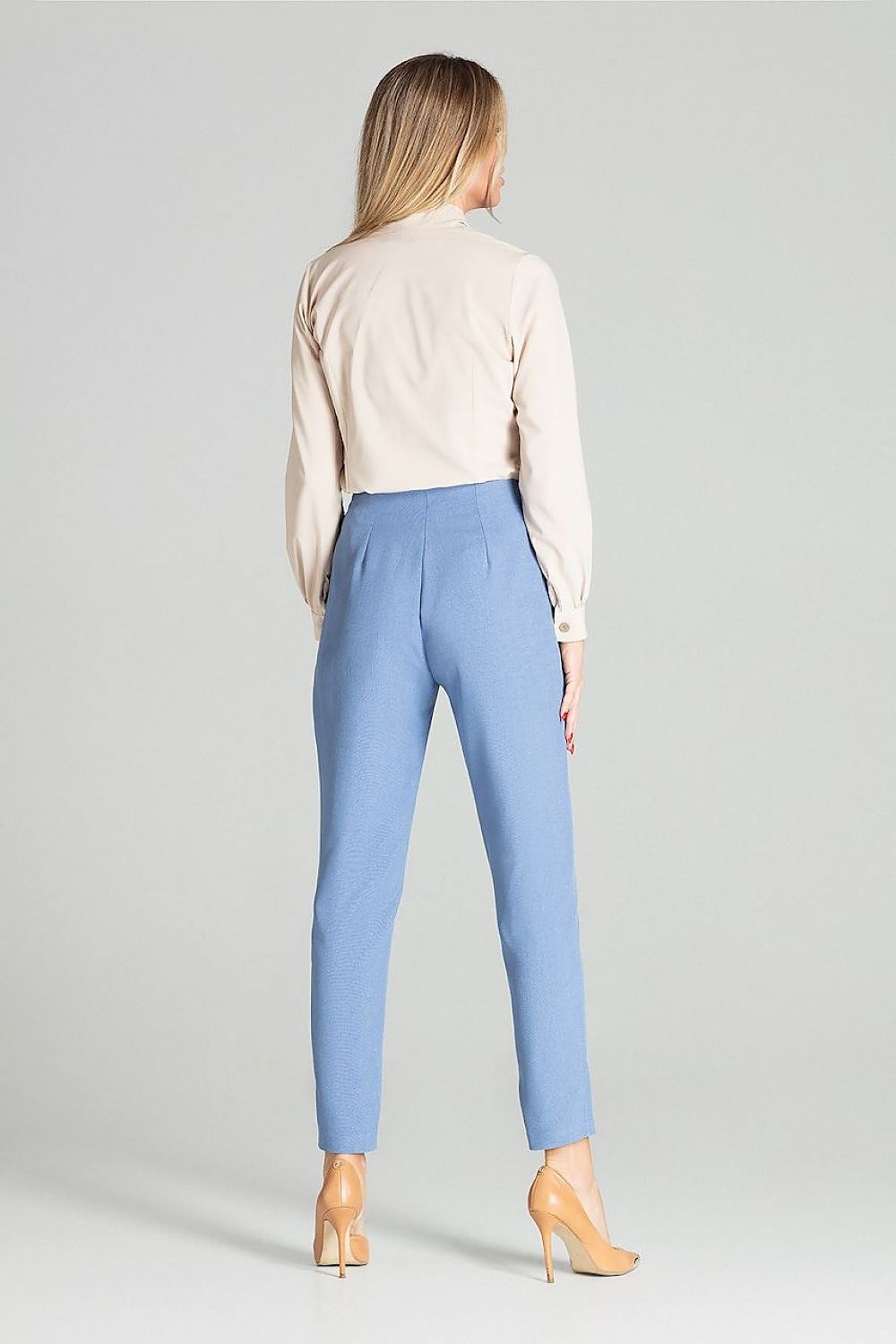 Woman wearing a beige blouse and blue pants on a gray background