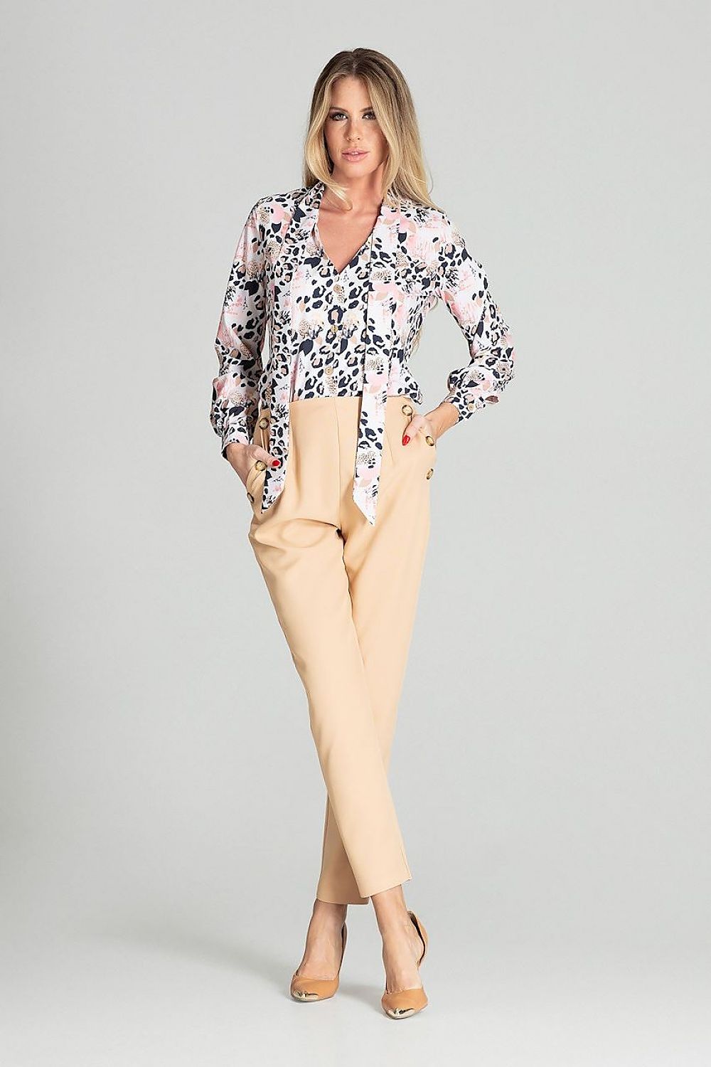 Woman wearing a patterned blouse and beige pants on a gray background