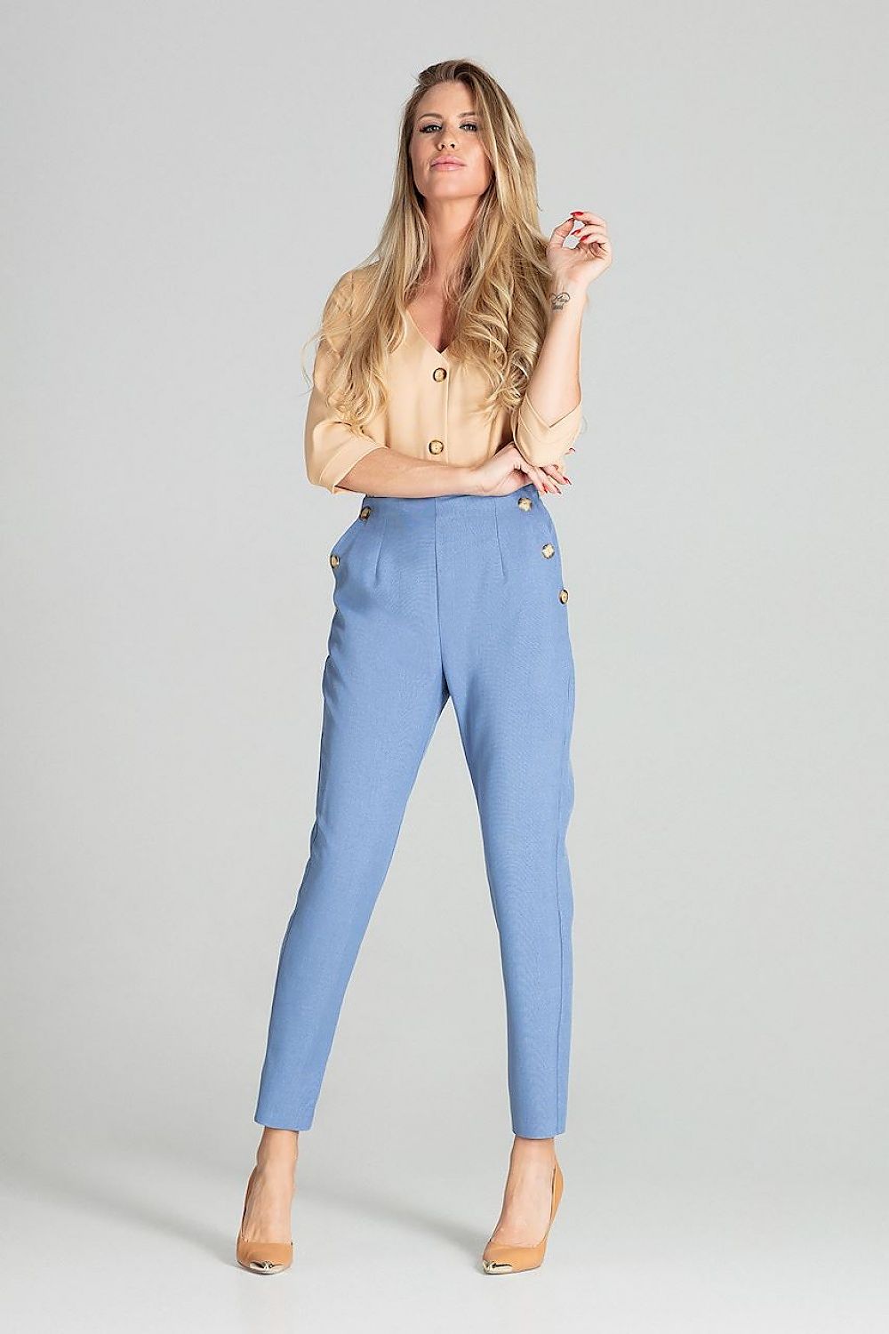 Woman wearing a beige blouse and blue pants on a gray background
