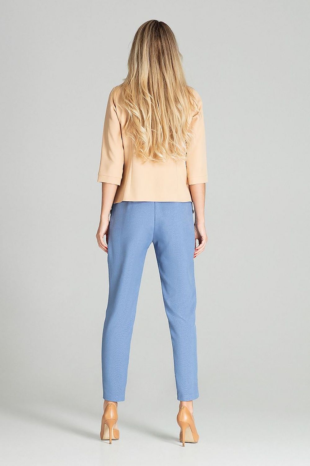 Woman wearing a beige top and blue pants on a gray background