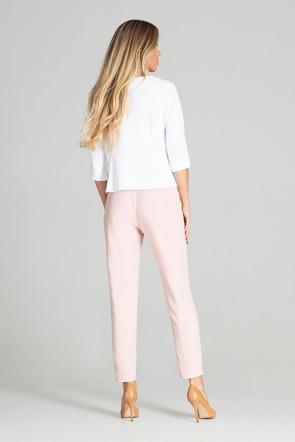 Woman wearing a white top and pink pants on a gray background
