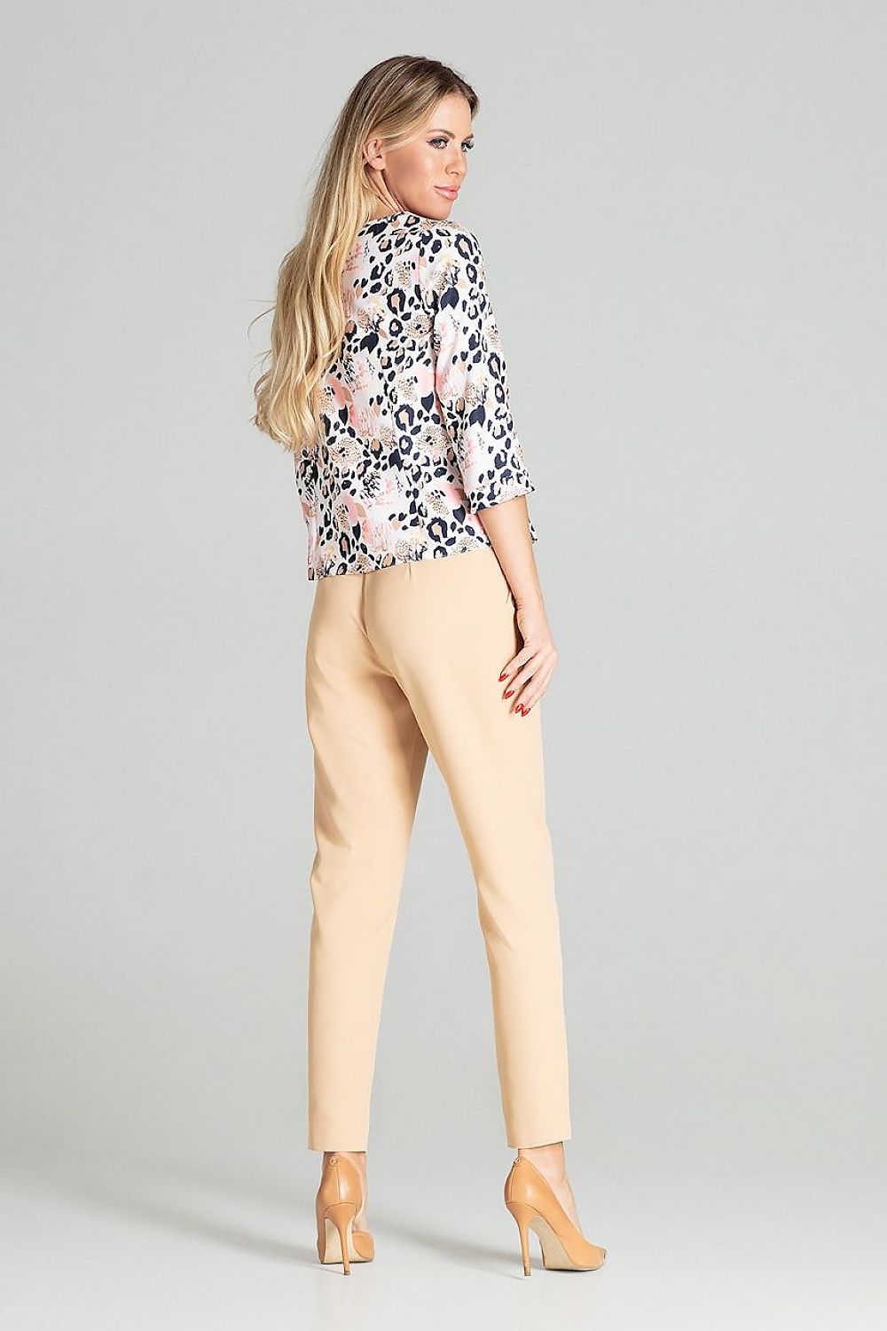 Woman wearing a floral blouse and beige pants on a gray background