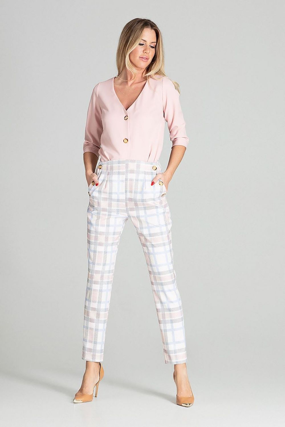 Woman wearing a pink cardigan and checkered pants on a gray background