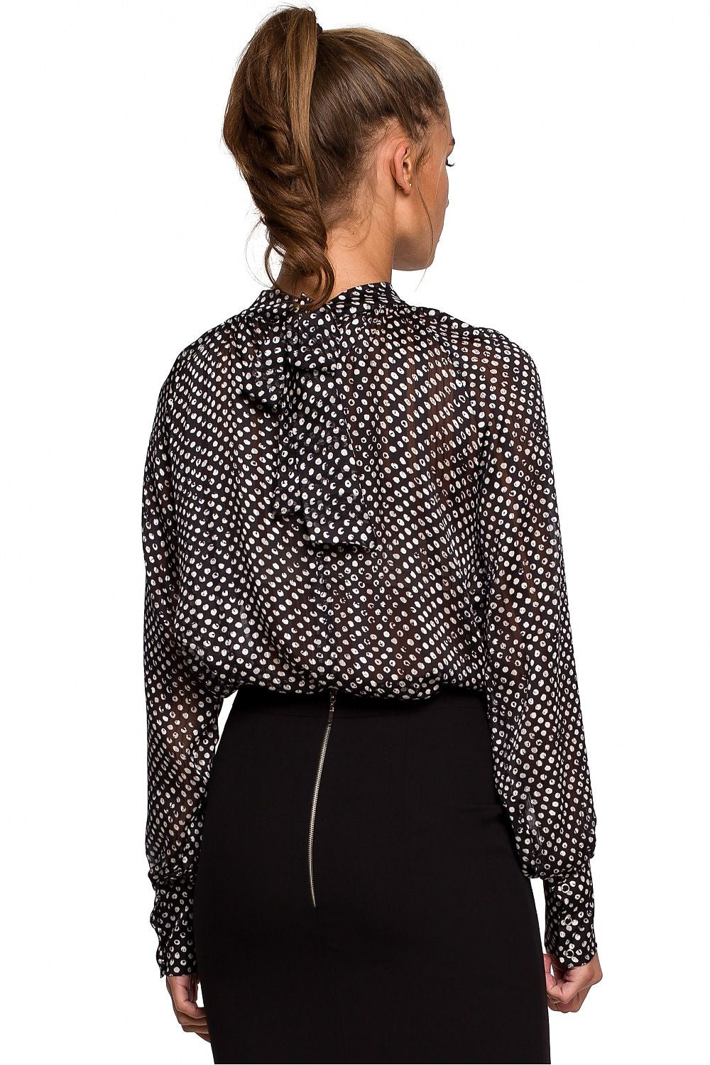 Woman wearing a black and white polka dot blouse with long sleeves on a white background