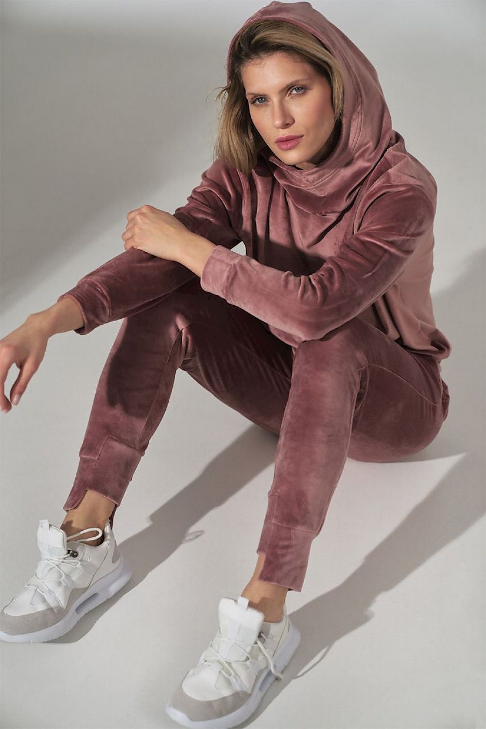 Woman wearing a mauve tracksuit with white sneakers on a light gray background
