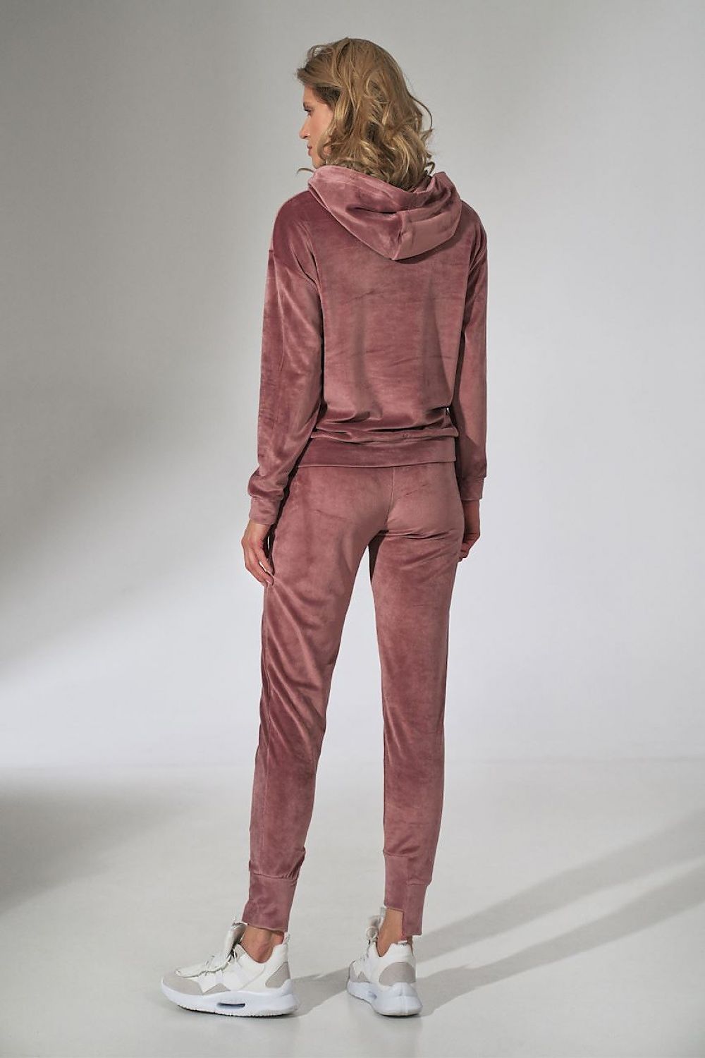 Person wearing a pink velour tracksuit on a plain background