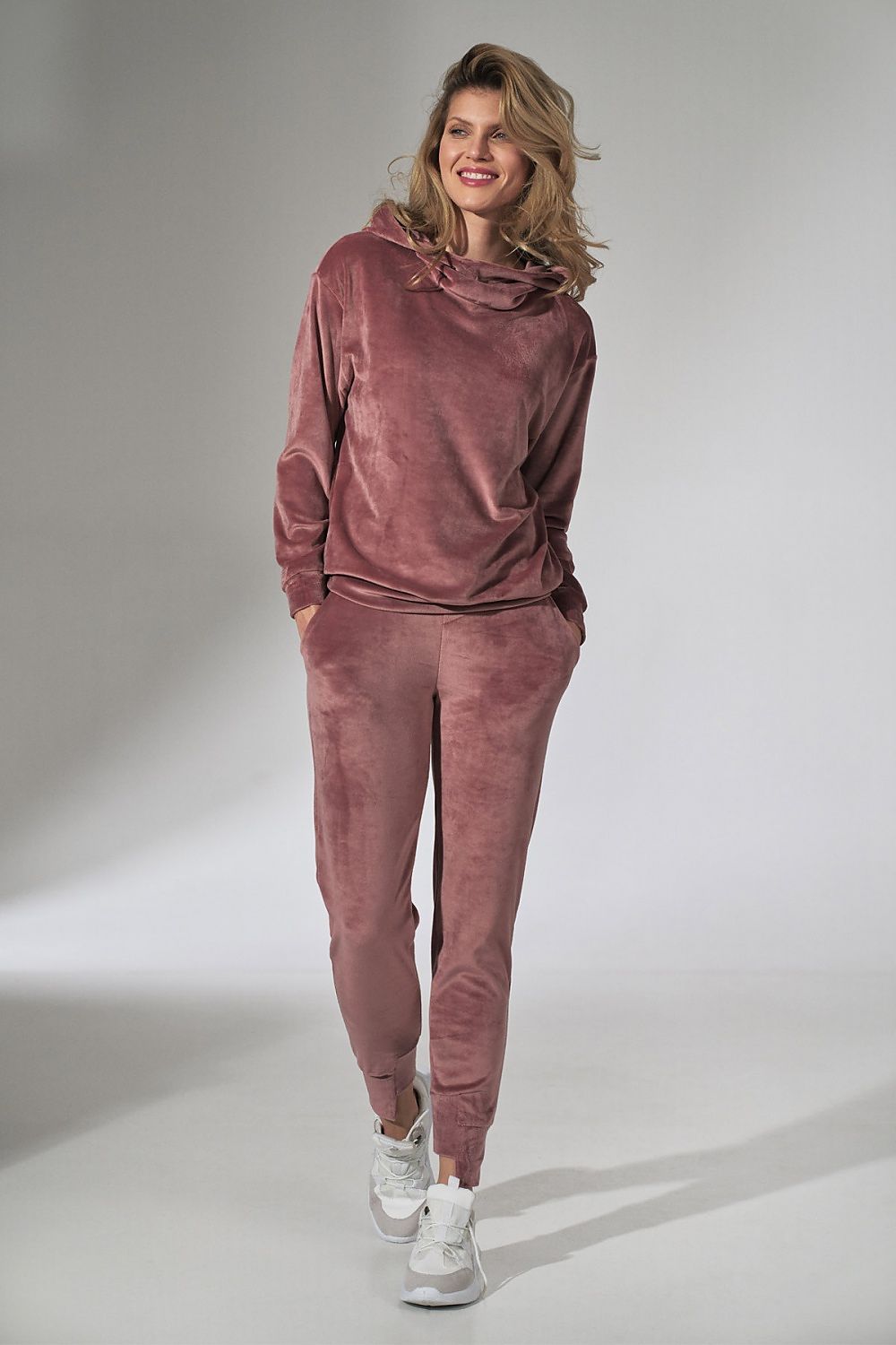 Woman wearing a pink velour tracksuit on a gray background