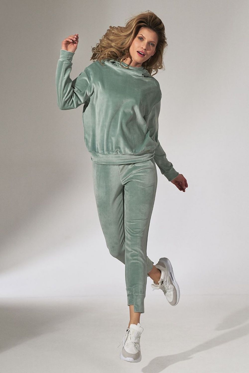 Woman wearing a green velvet tracksuit on a plain background