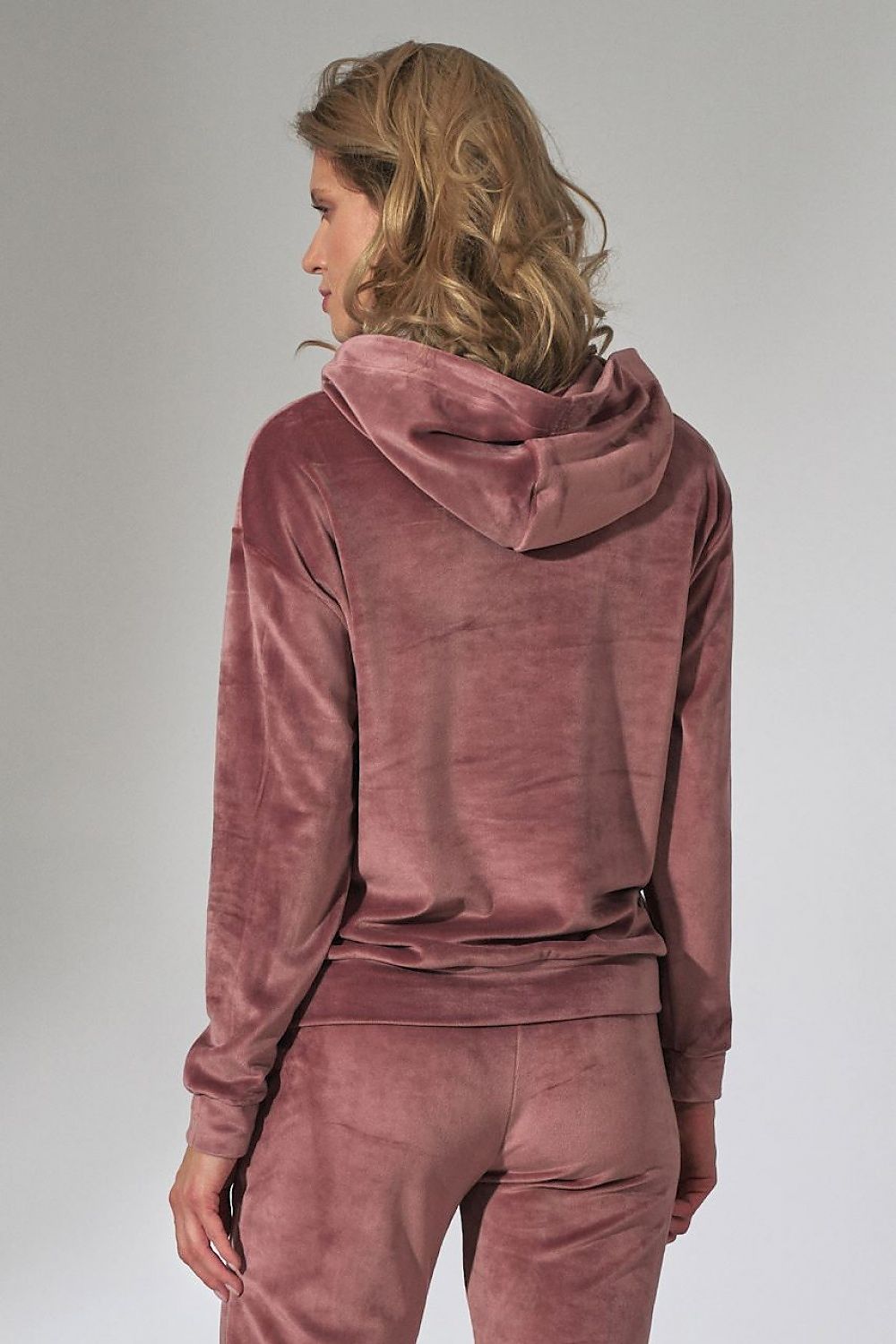 Person wearing a mauve velour tracksuit on a plain background
