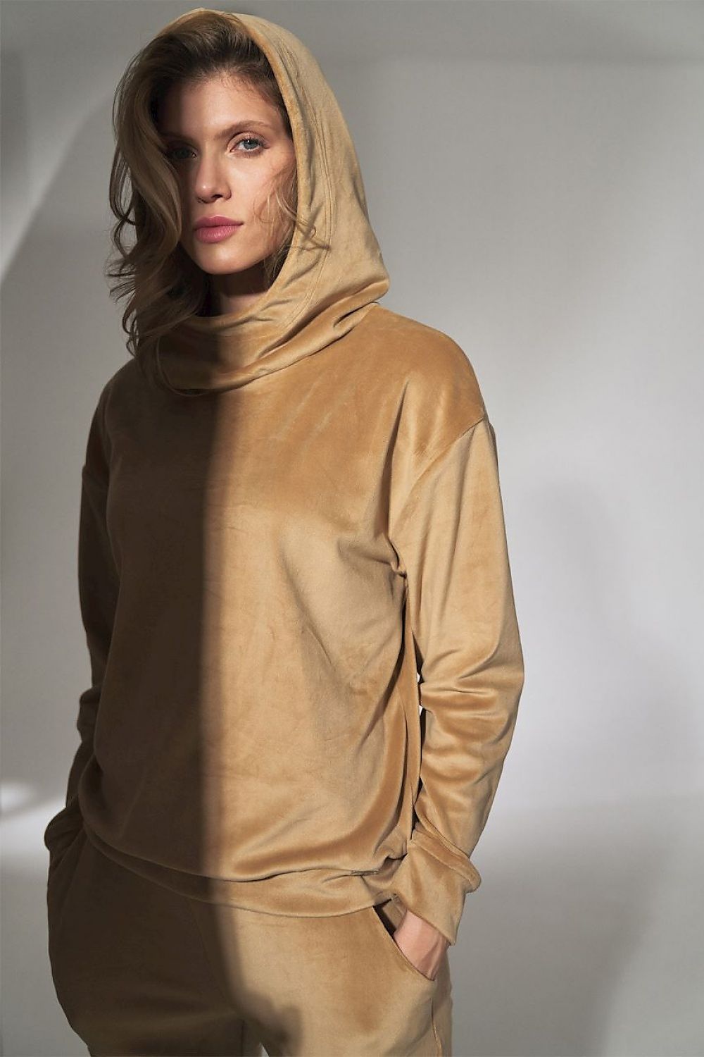 Person wearing a beige hoodie and pants against a neutral background
