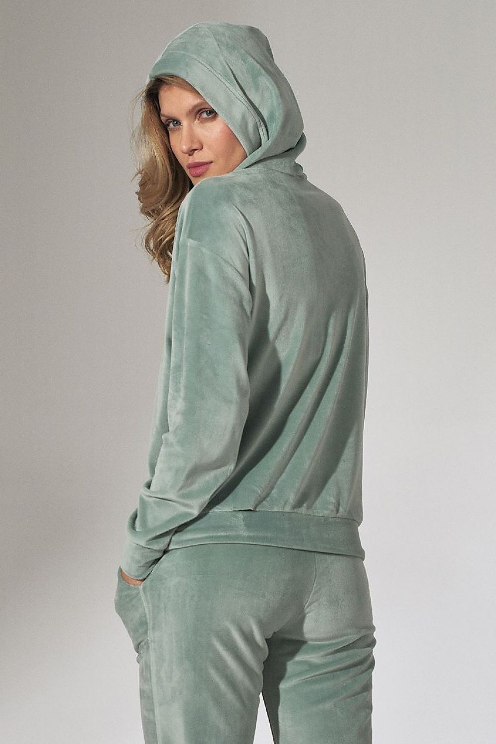 Woman wearing a light green velour tracksuit against a plain background