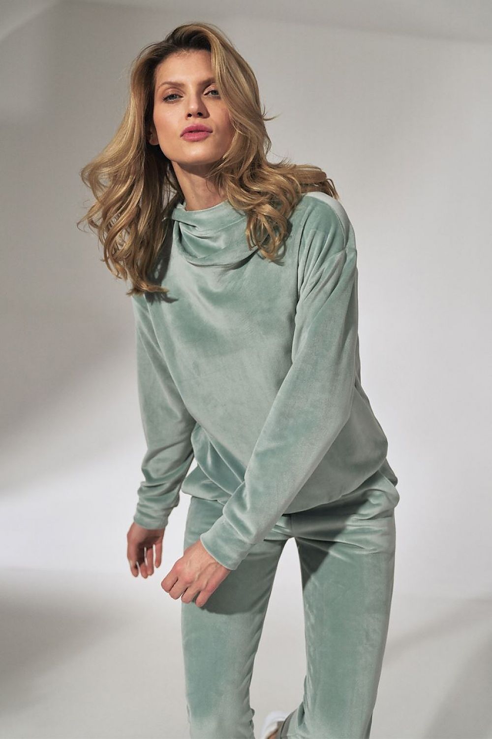 Woman wearing a light green velvet outfit on a plain background