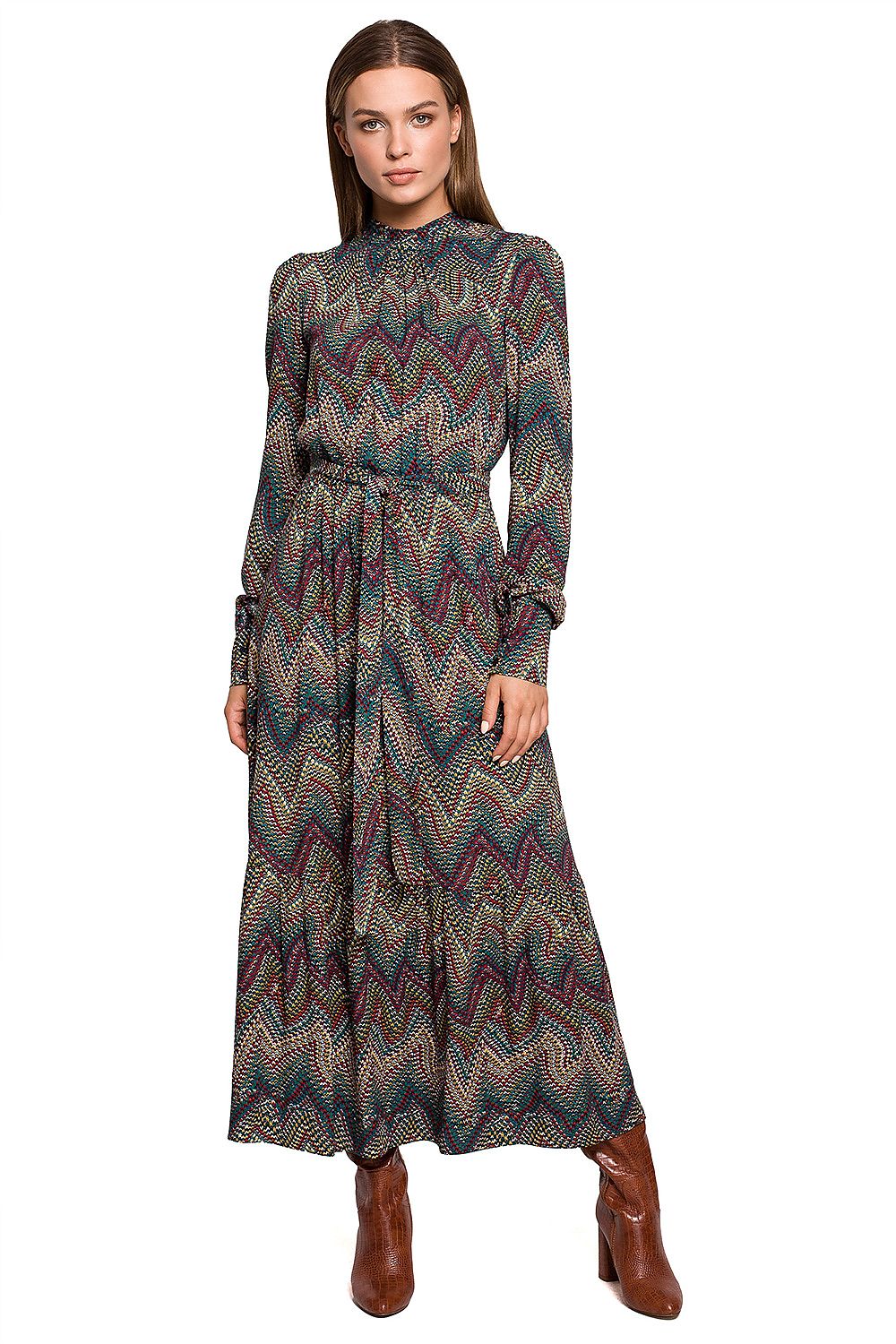 Woman wearing a long, patterned dress with brown boots on a white background