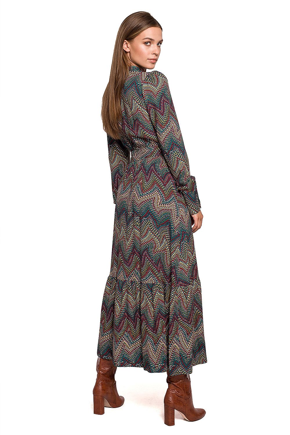 Woman wearing a long, patterned dress with brown boots on a white background