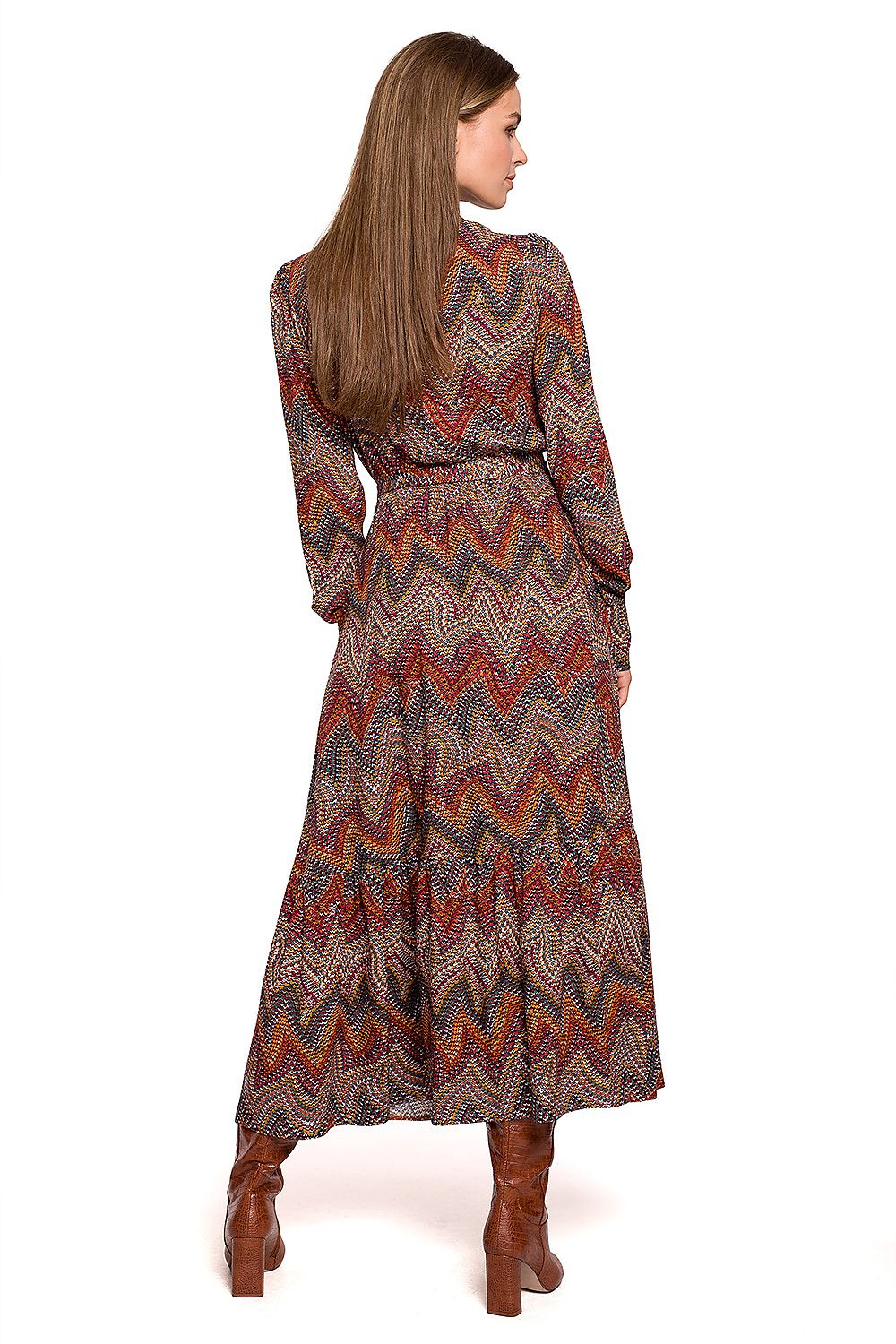A woman shown from the back wearing a long-sleeve maxi dress with a multicolor chevron pattern in brown, orange, red, and beige, paired with brown leather boots, against a plain white background.