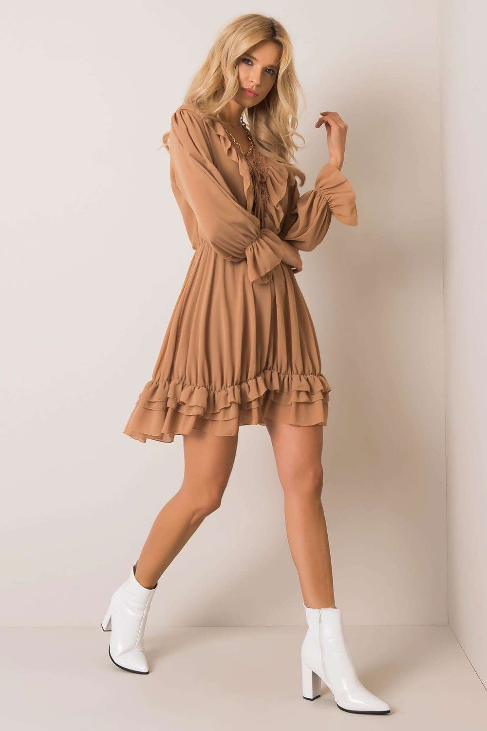 Woman wearing a brown dress with ruffles and white boots on a plain background