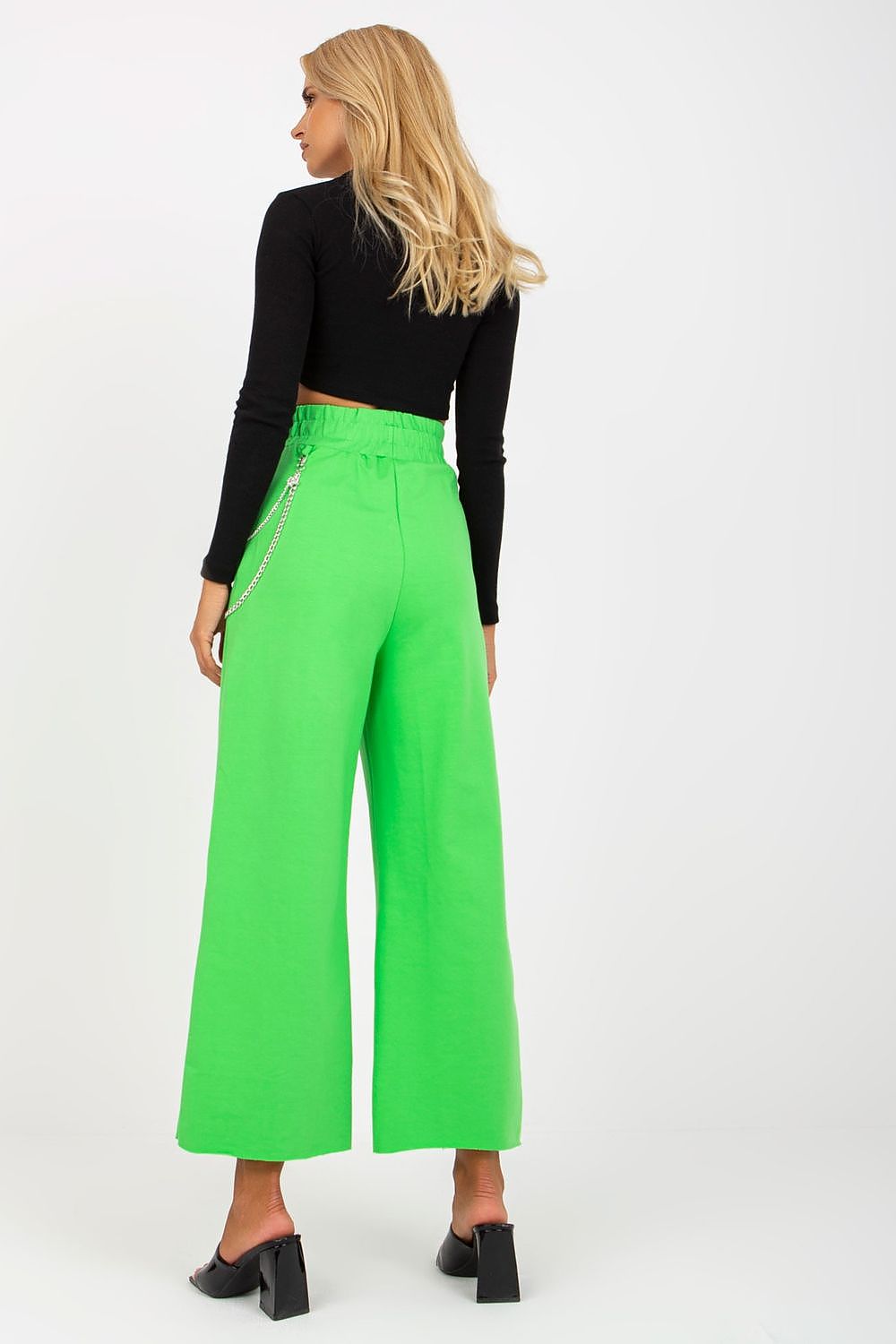 Woman wearing bright green wide-leg pants and a black top on a white background