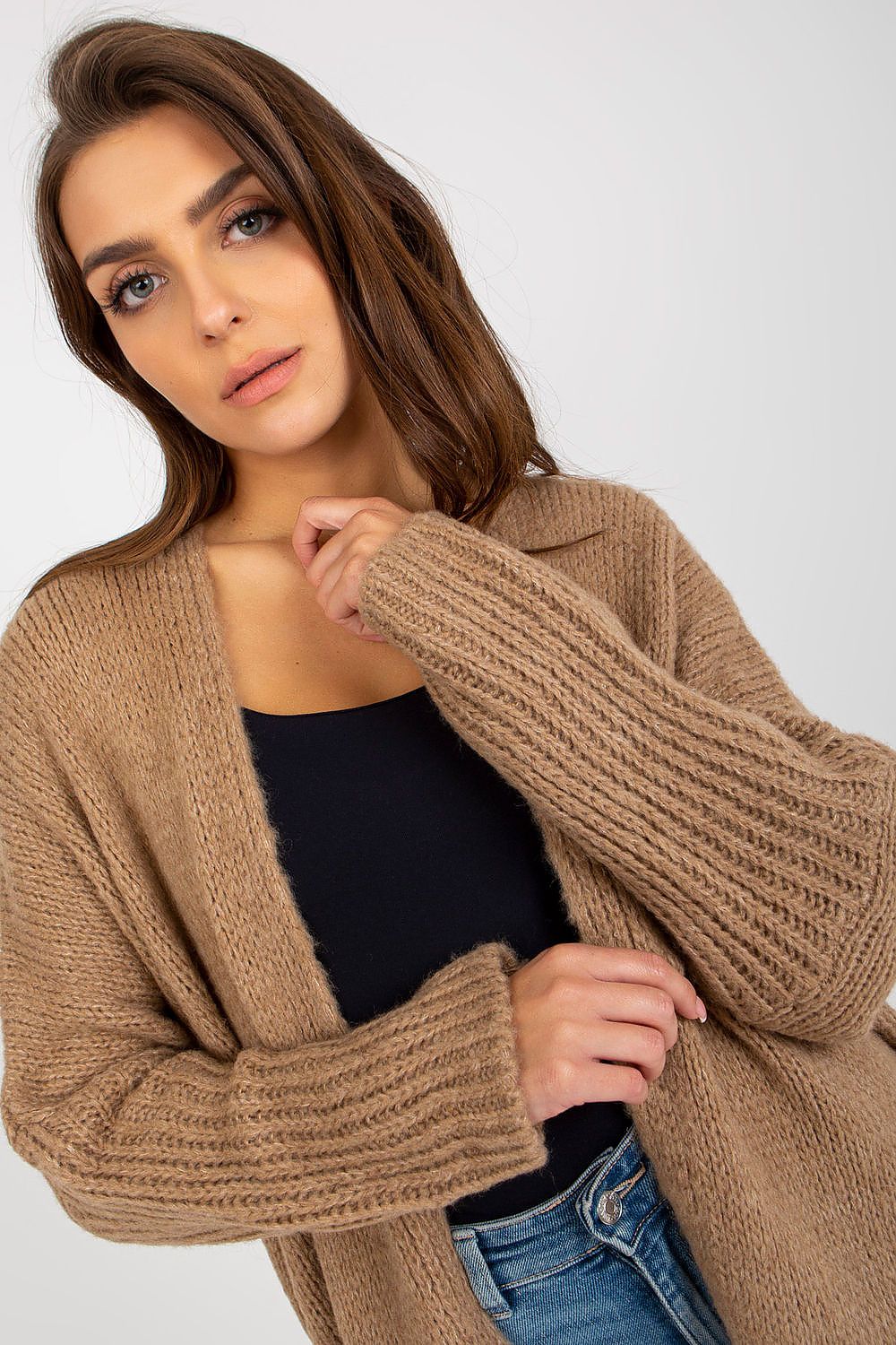 Woman wearing a beige cardigan over a black top and blue jeans on a white background