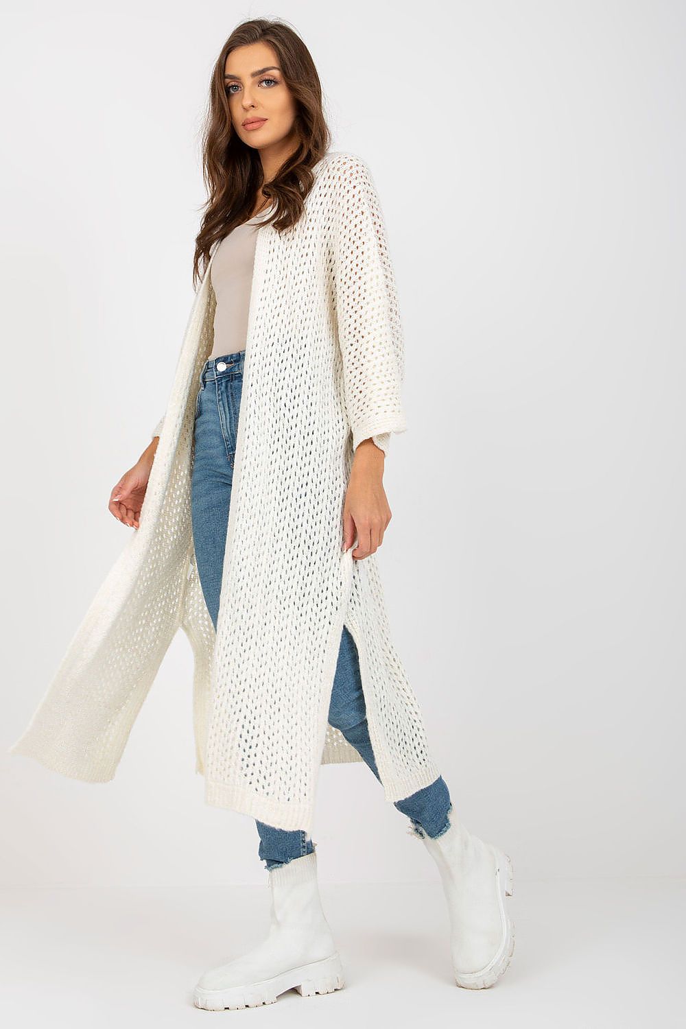 Woman wearing a long cream cardigan over a white top and blue jeans on a white background