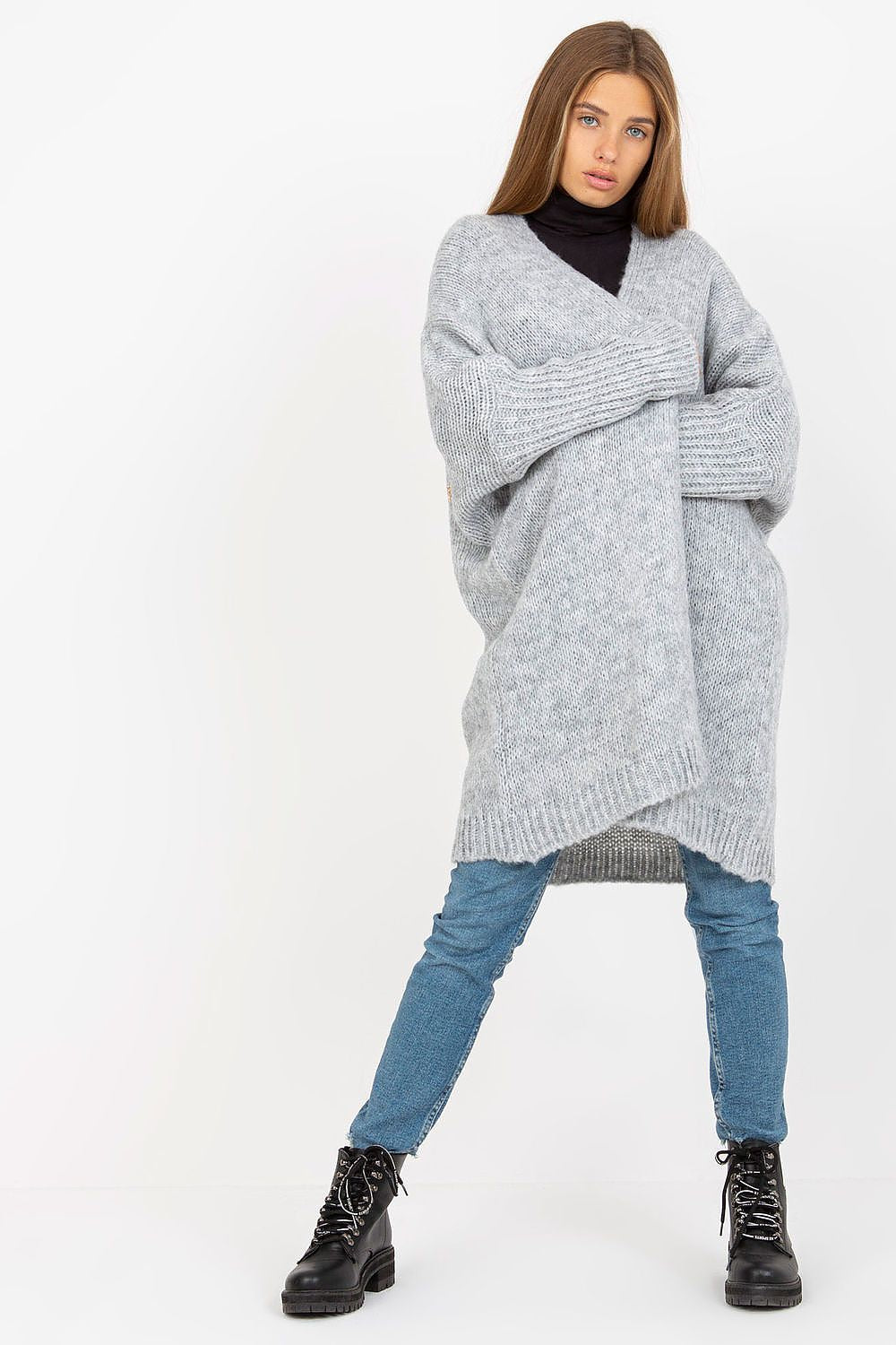 Person wearing a large gray knitted sweater with blue jeans on a white background