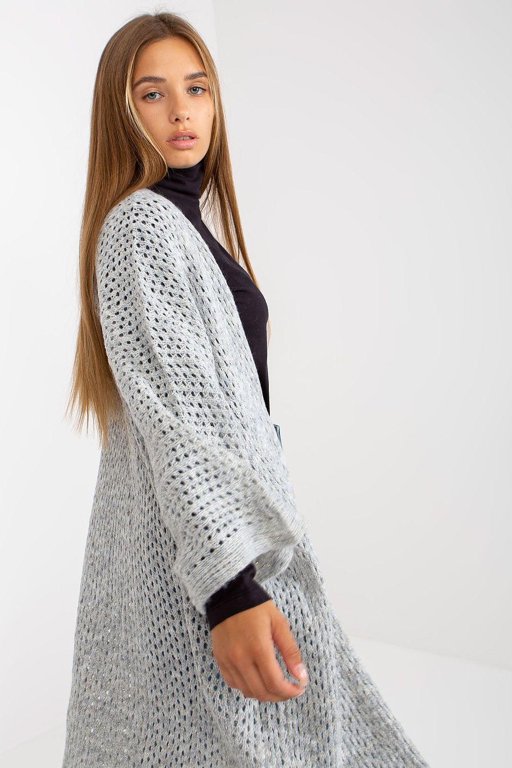 Woman wearing a long, light gray knitted cardigan over a black top on a white background