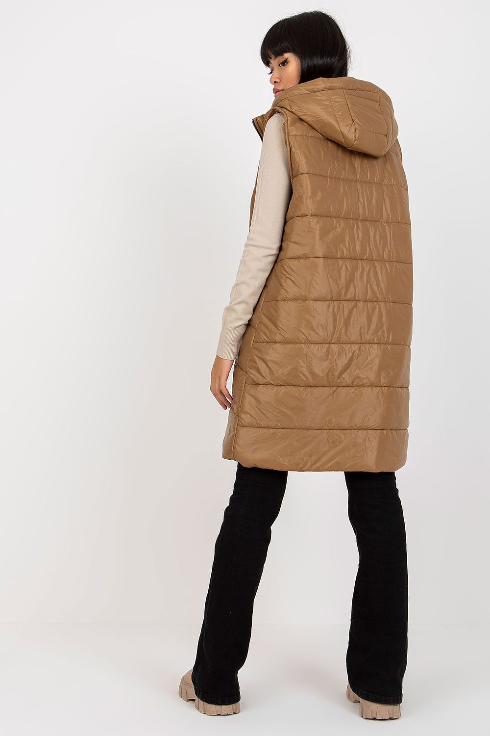 Woman wearing a long brown puffer vest on a white background