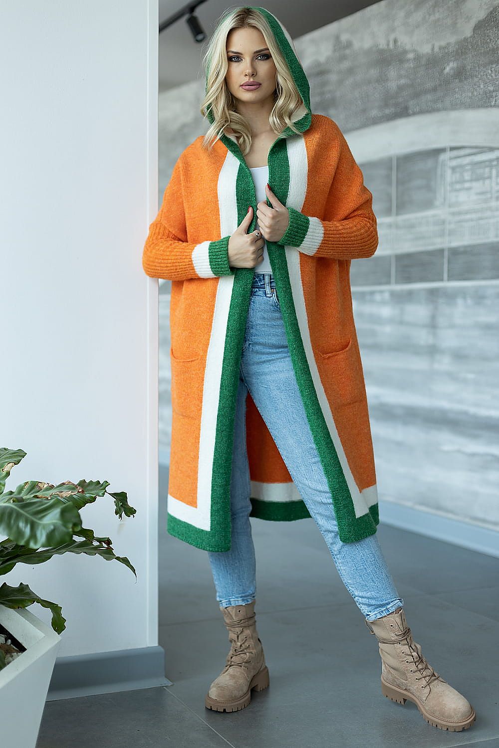 Woman wearing an orange, green, and white coat with a hood in an indoor setting.