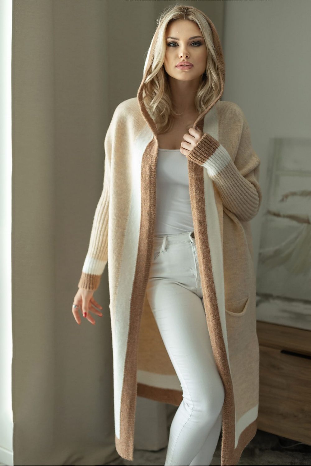 Woman wearing a long beige cardigan over a white outfit in a neutral setting