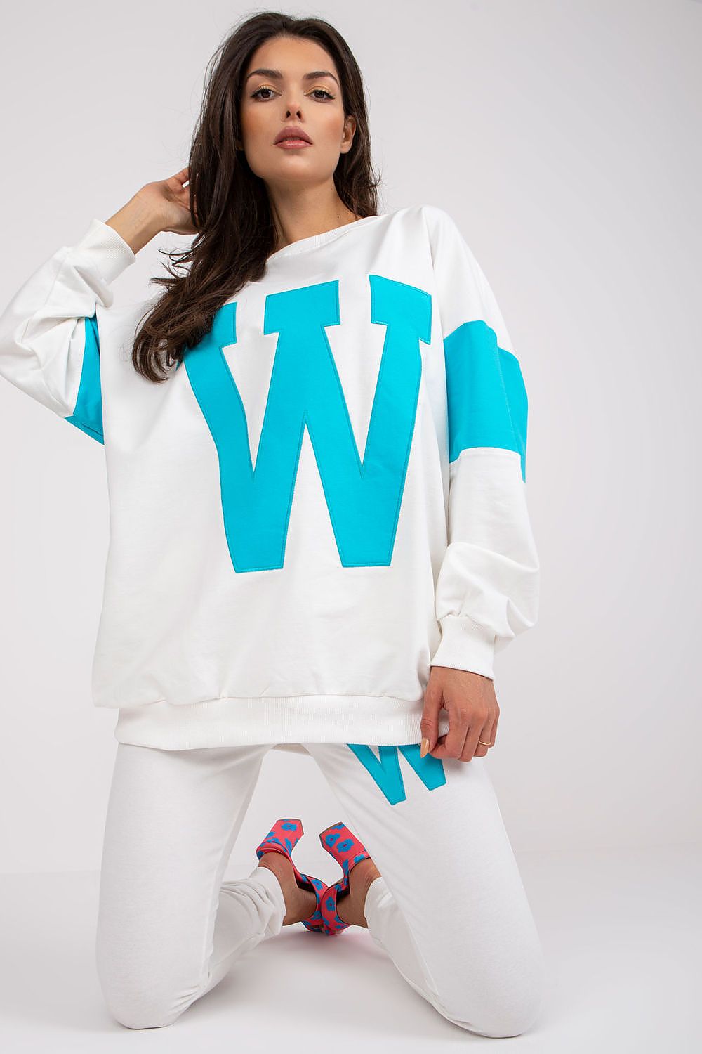 Woman wearing a white sweatshirt with large blue 'W's on a plain background