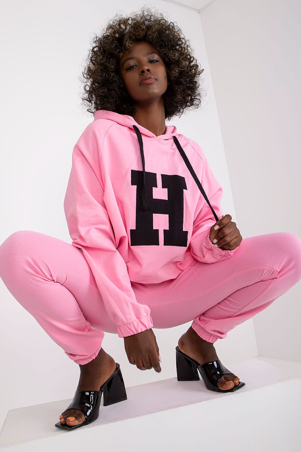 Person wearing a pink hoodie and pants with a large black letter 'H' on a white background