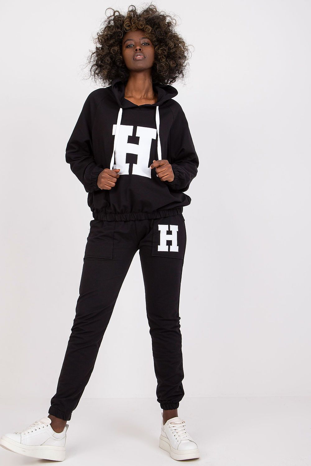 Person wearing a black hoodie and jogger set with 'H' logo on a white background