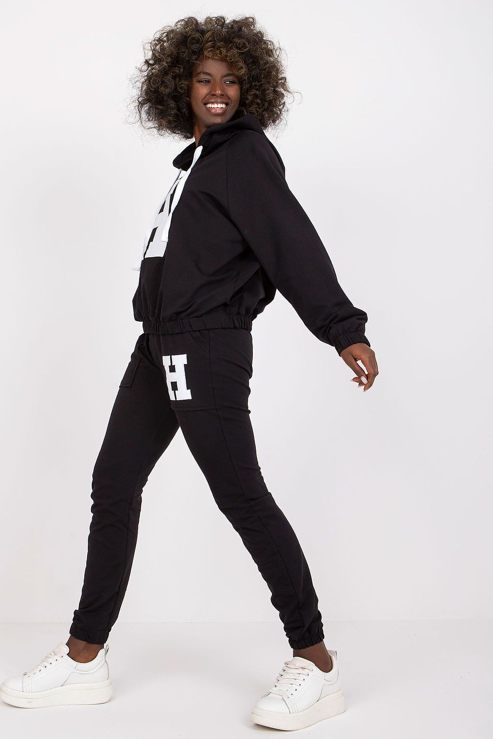 Person wearing a black tracksuit with a logo on a white background
