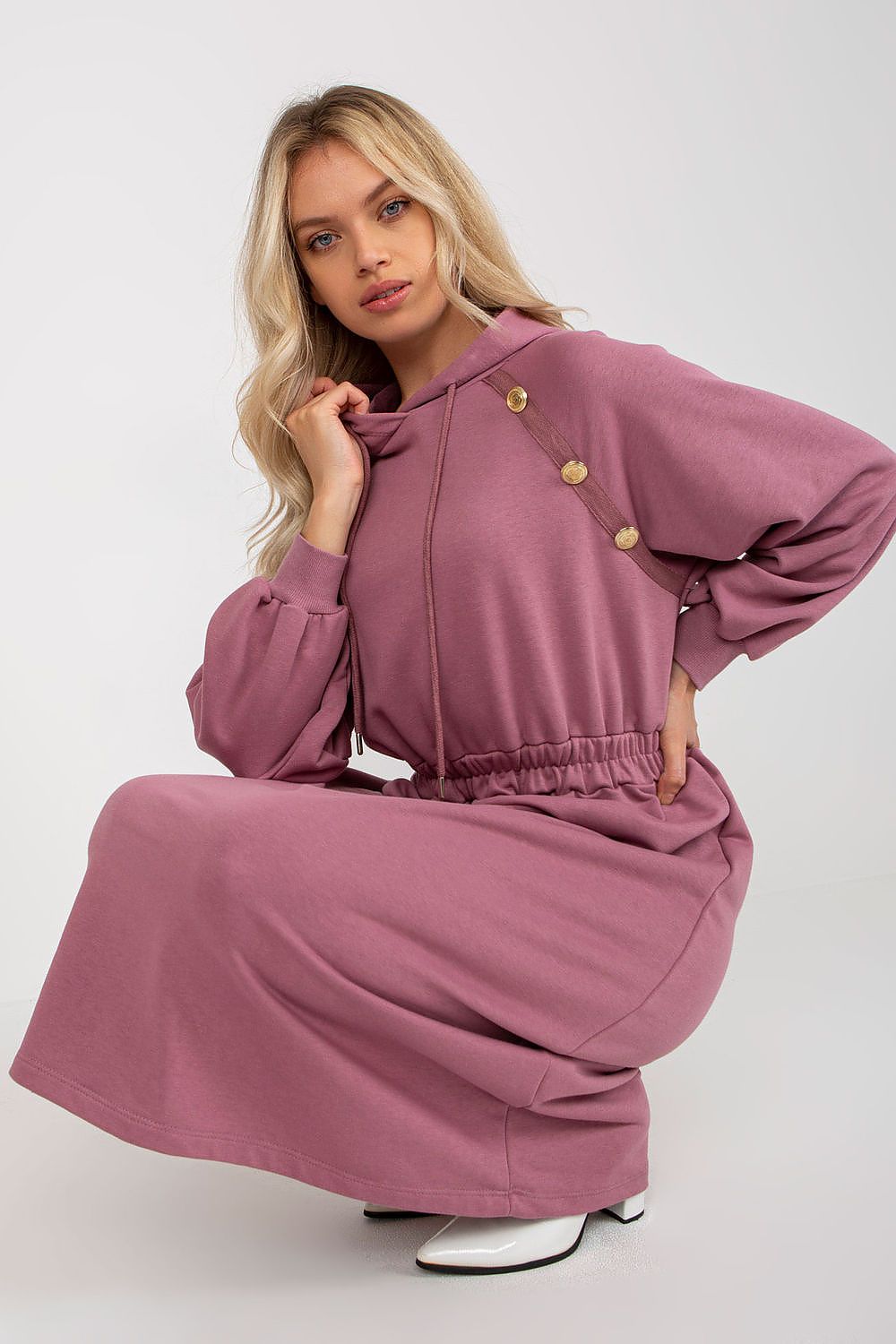 Woman wearing a mauve outfit with gold buttons on a white background