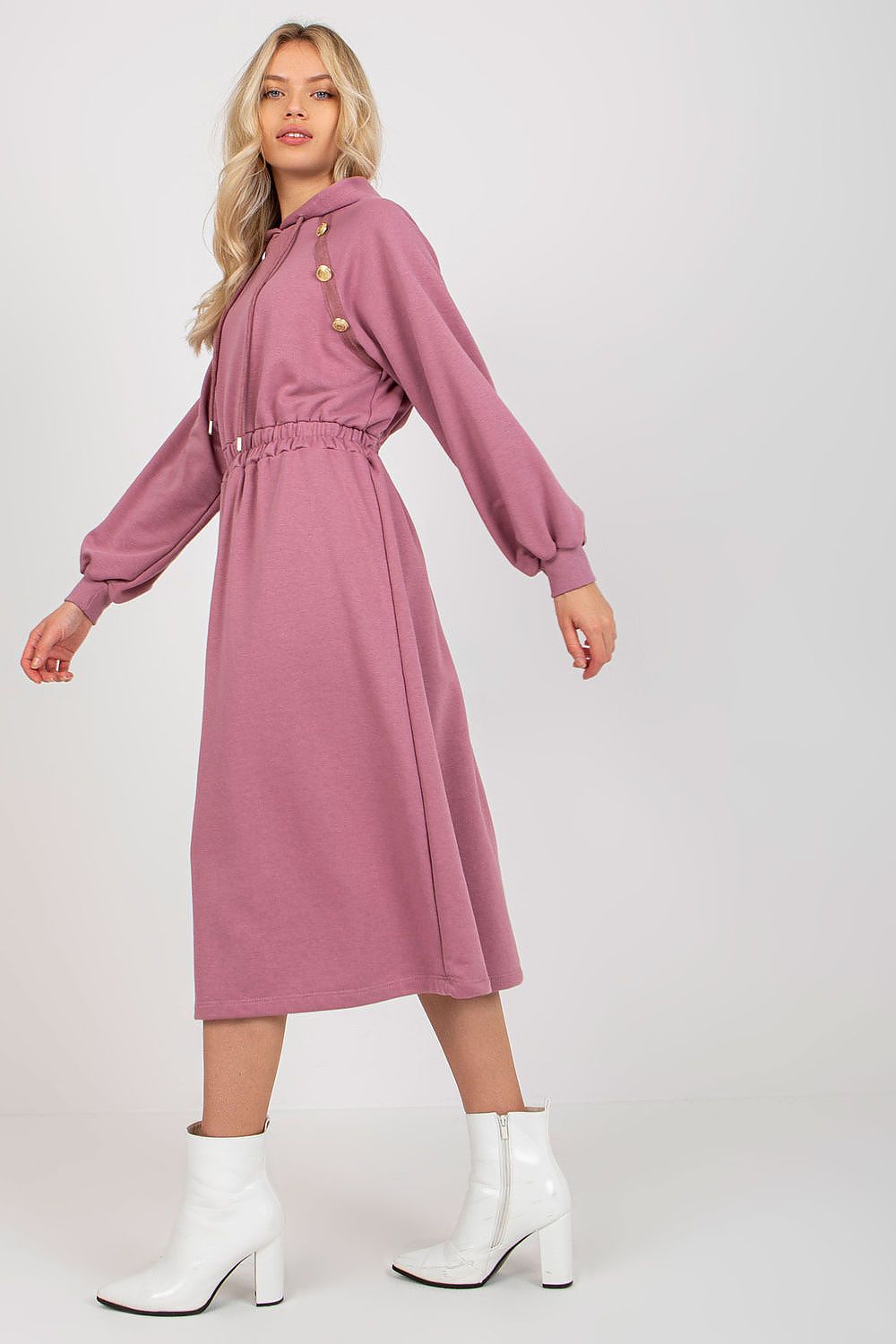 Woman wearing a pink dress with button details and white boots on a white background