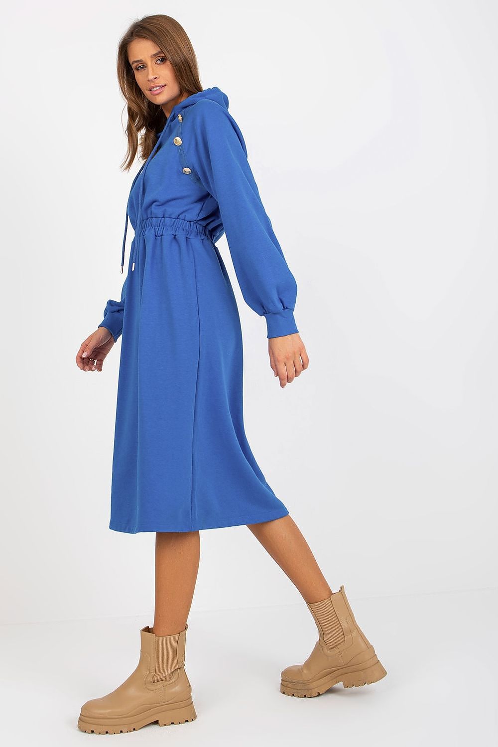 Woman wearing a blue dress with a belt and beige boots on a white background