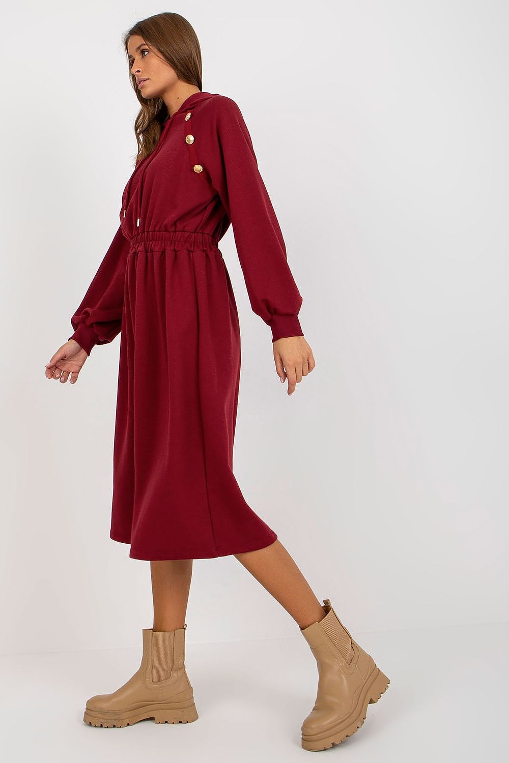 Woman wearing a burgundy dress with button details and beige boots on a white background