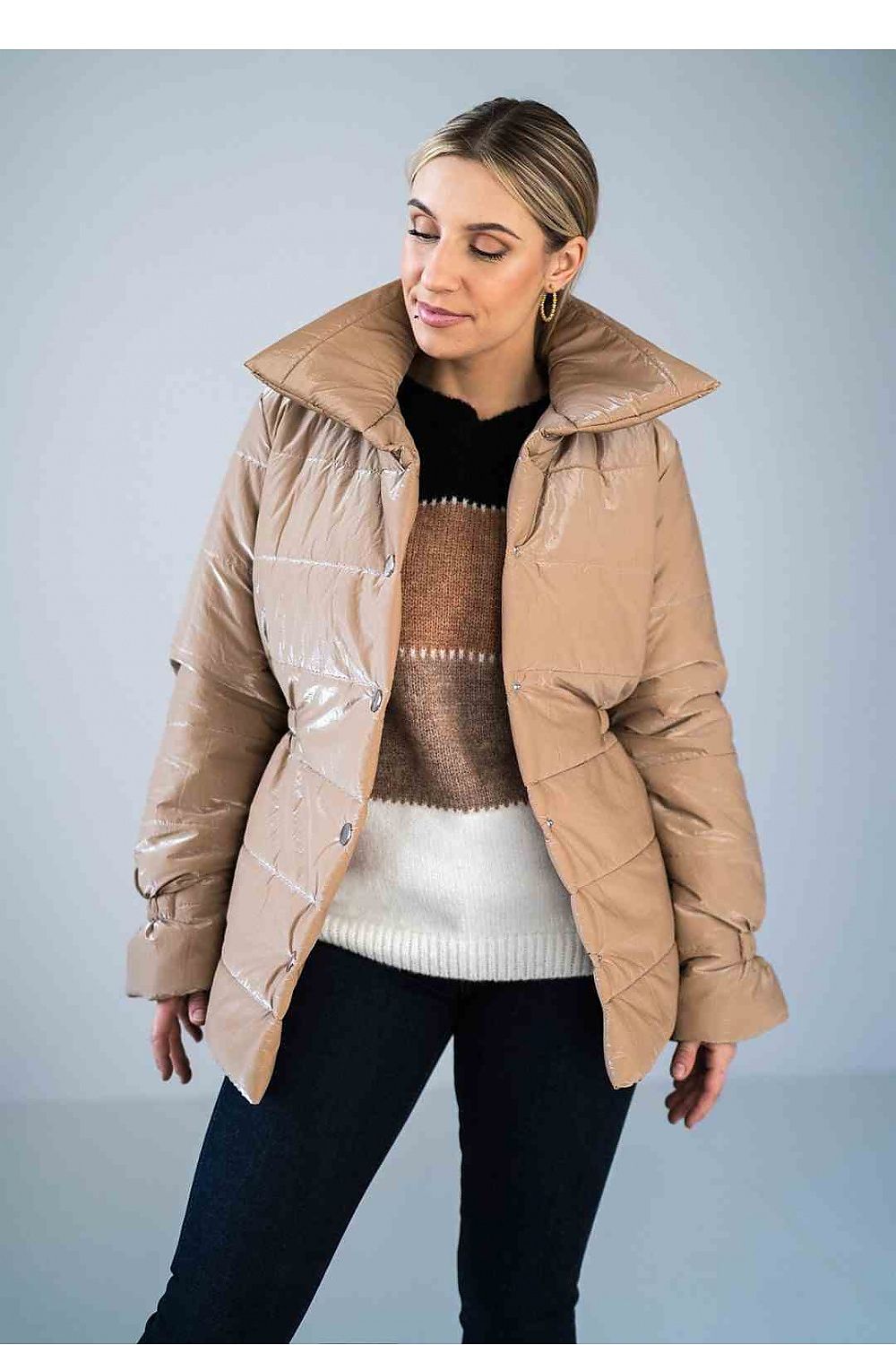 Woman wearing a beige puffer jacket over a sweater with a plain background