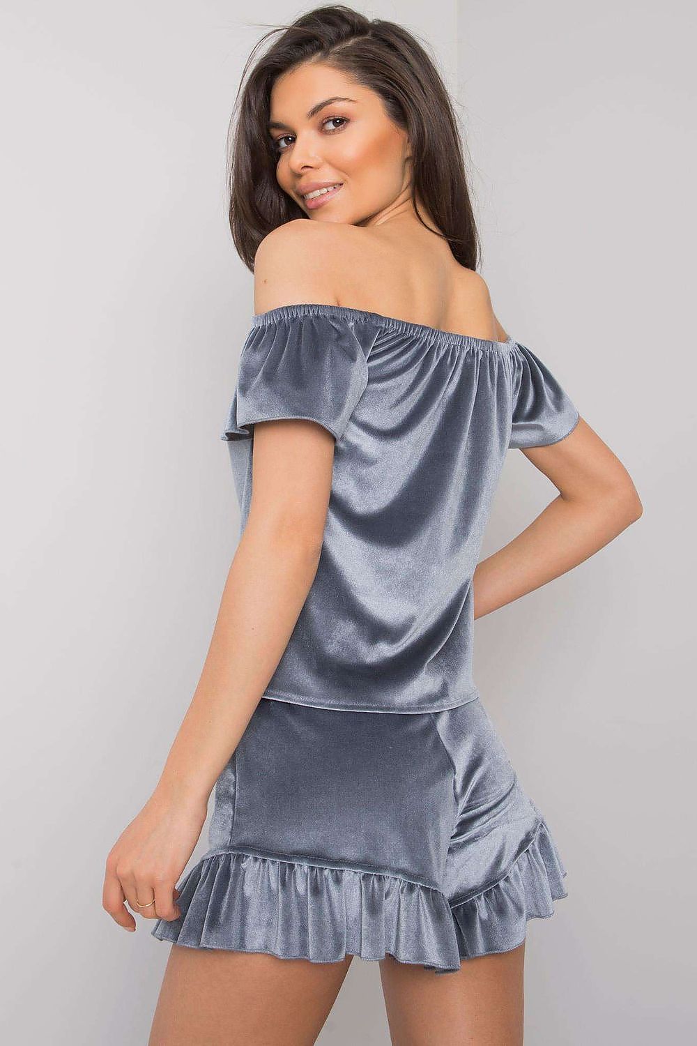 Woman wearing a gray velvet off-shoulder top and skirt set on a plain background