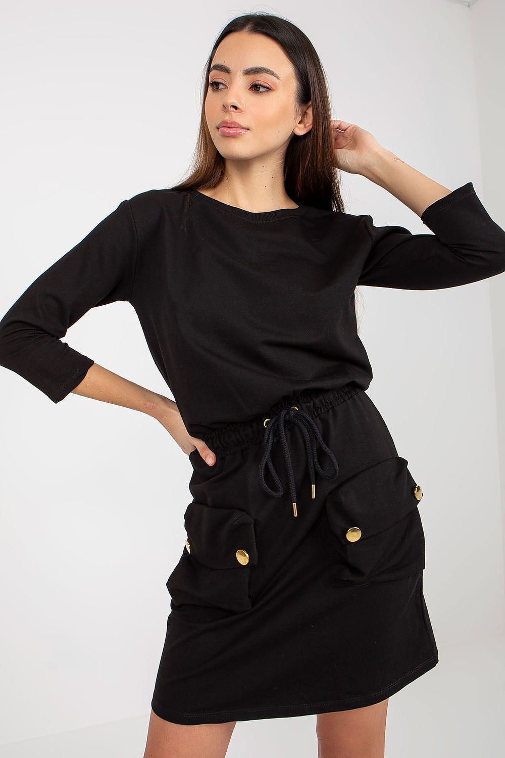 Woman wearing a black outfit with gold buttons on a white background