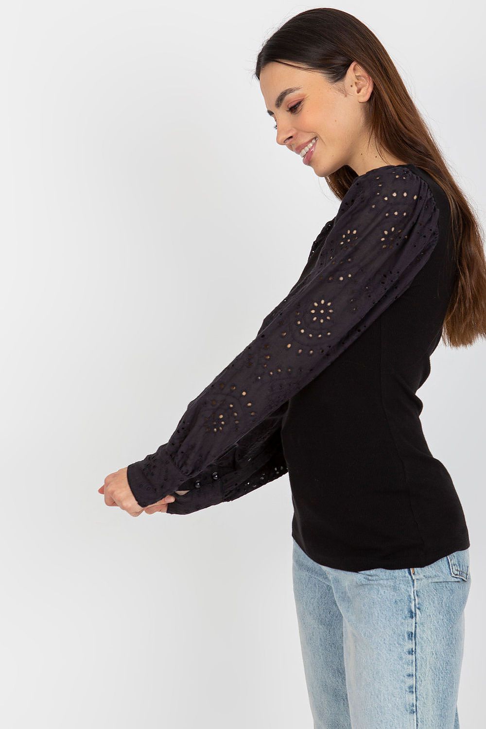 Woman wearing a black long-sleeve top with embellishments on a white background