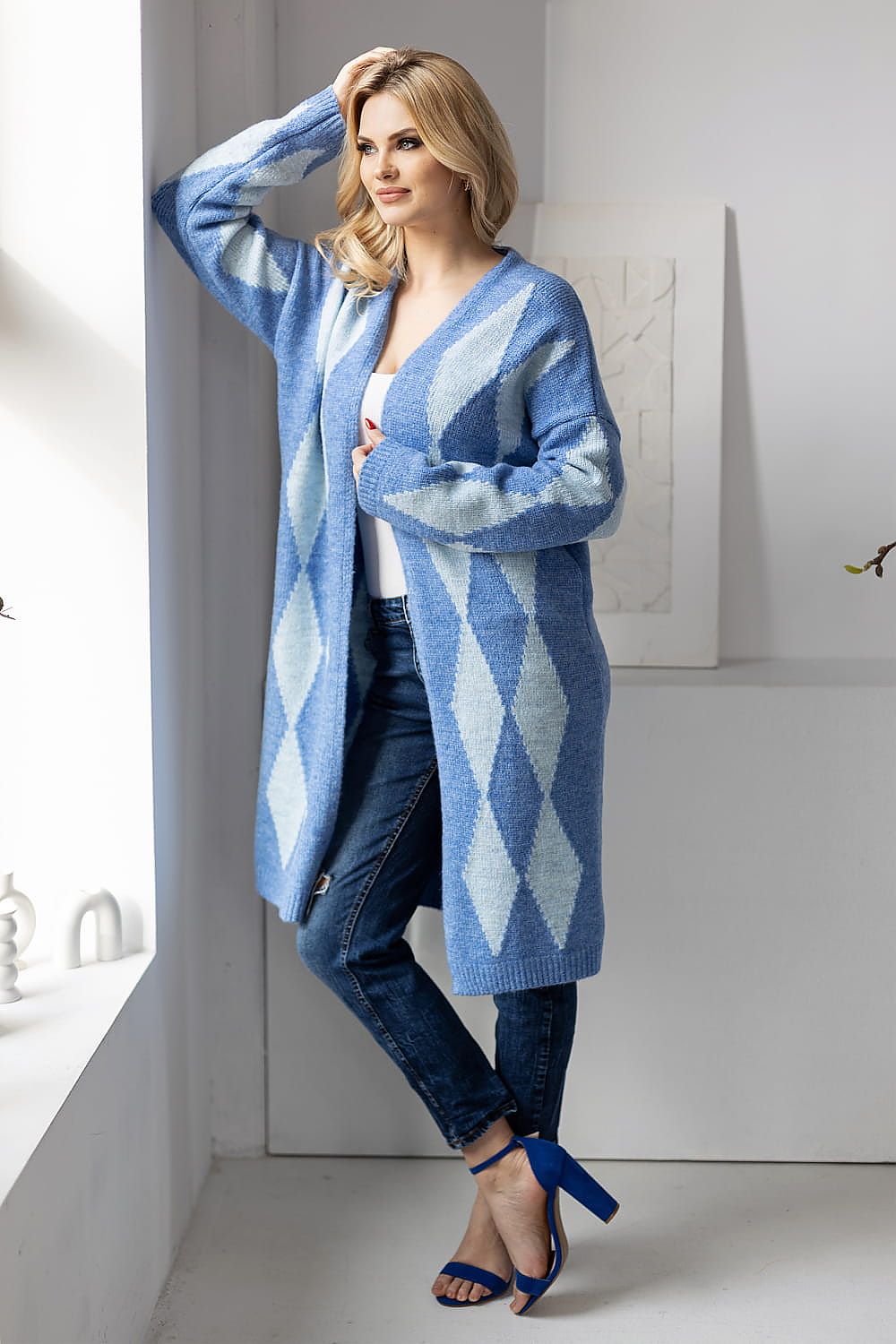 Woman wearing a long blue and white patterned cardigan in a minimalistic room.