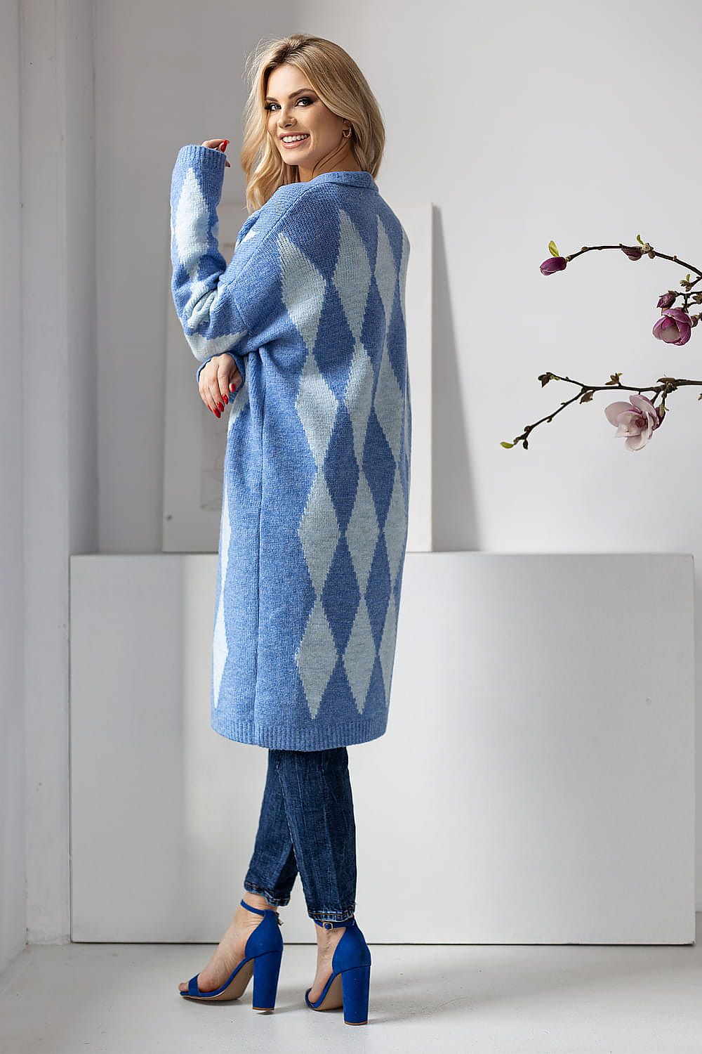 Woman wearing a blue argyle patterned coat in a minimalistic setting.