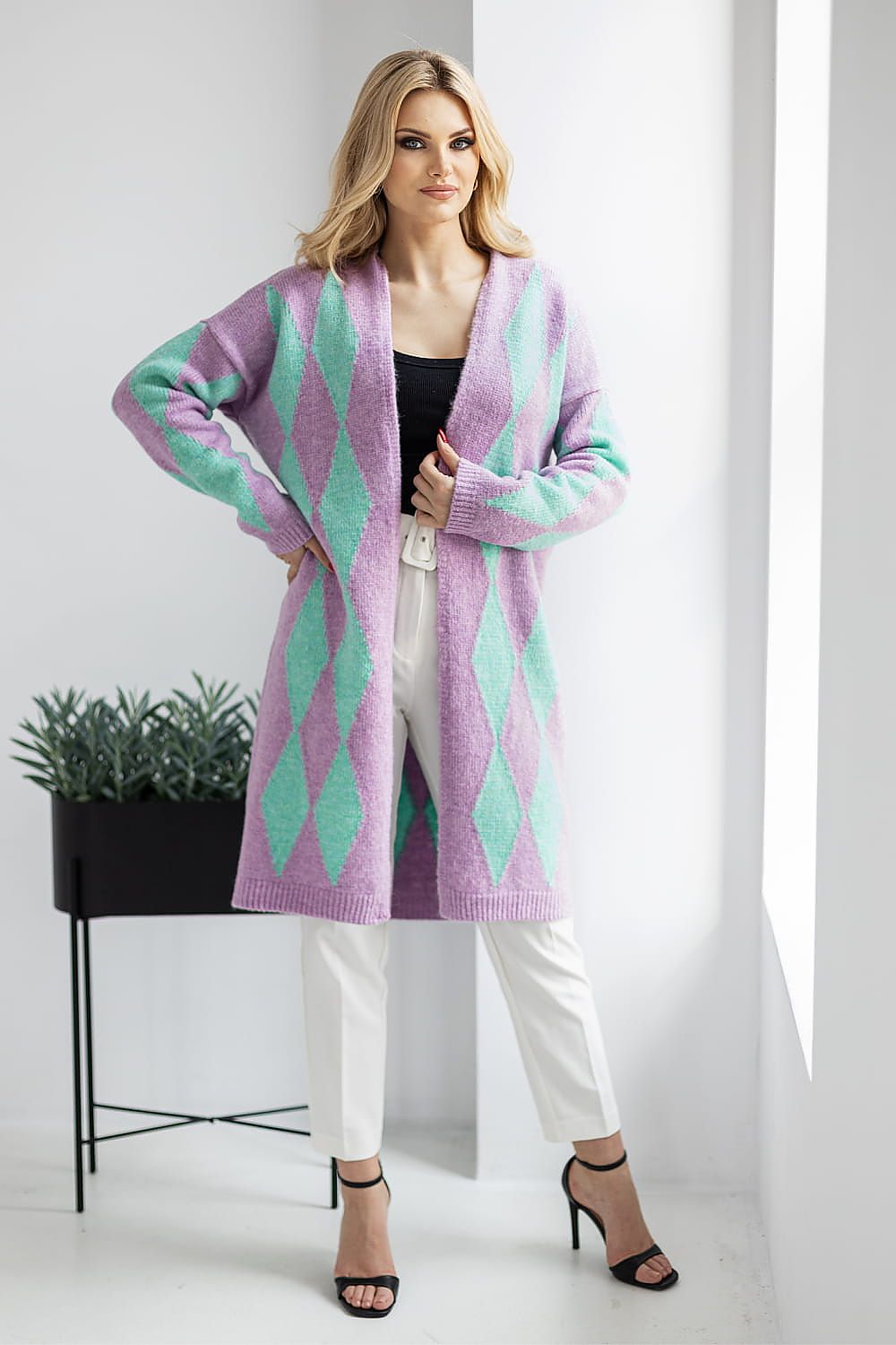 Woman wearing a long, patterned cardigan in a minimalistic setting