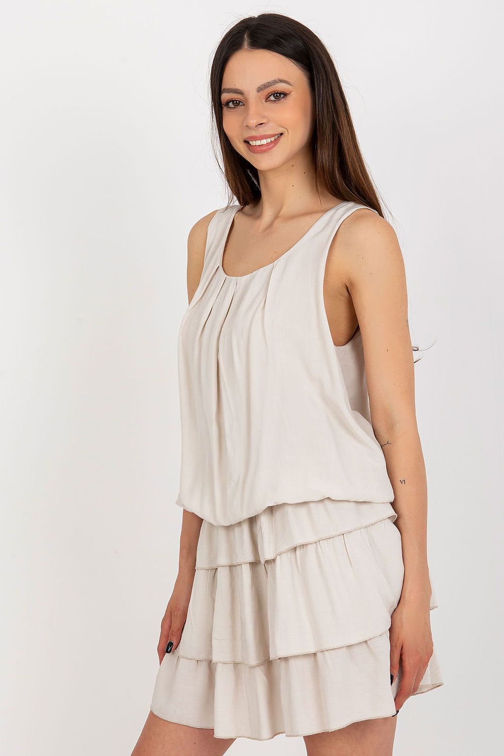 Woman wearing a beige sleeveless dress with layered skirt on a white background