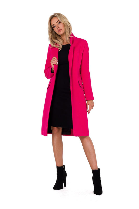Woman wearing a bright pink coat over a black dress on a white background