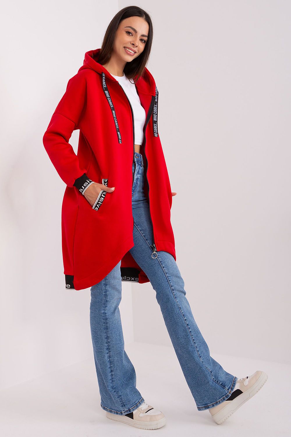 Woman wearing a red coat with black accents, white shirt, and blue jeans on a white background