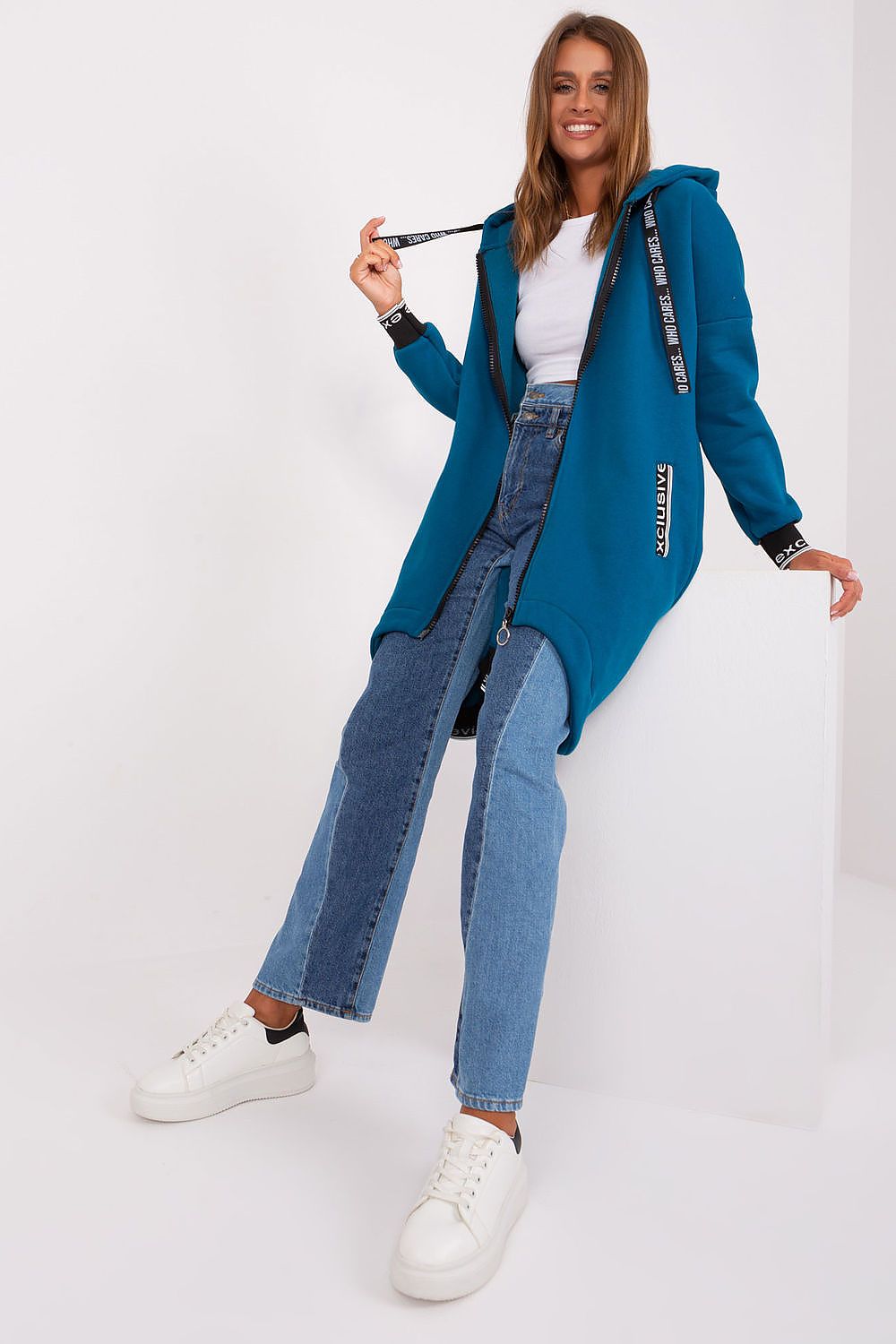 Woman wearing a blue cardigan, white shirt, and jeans on a white background