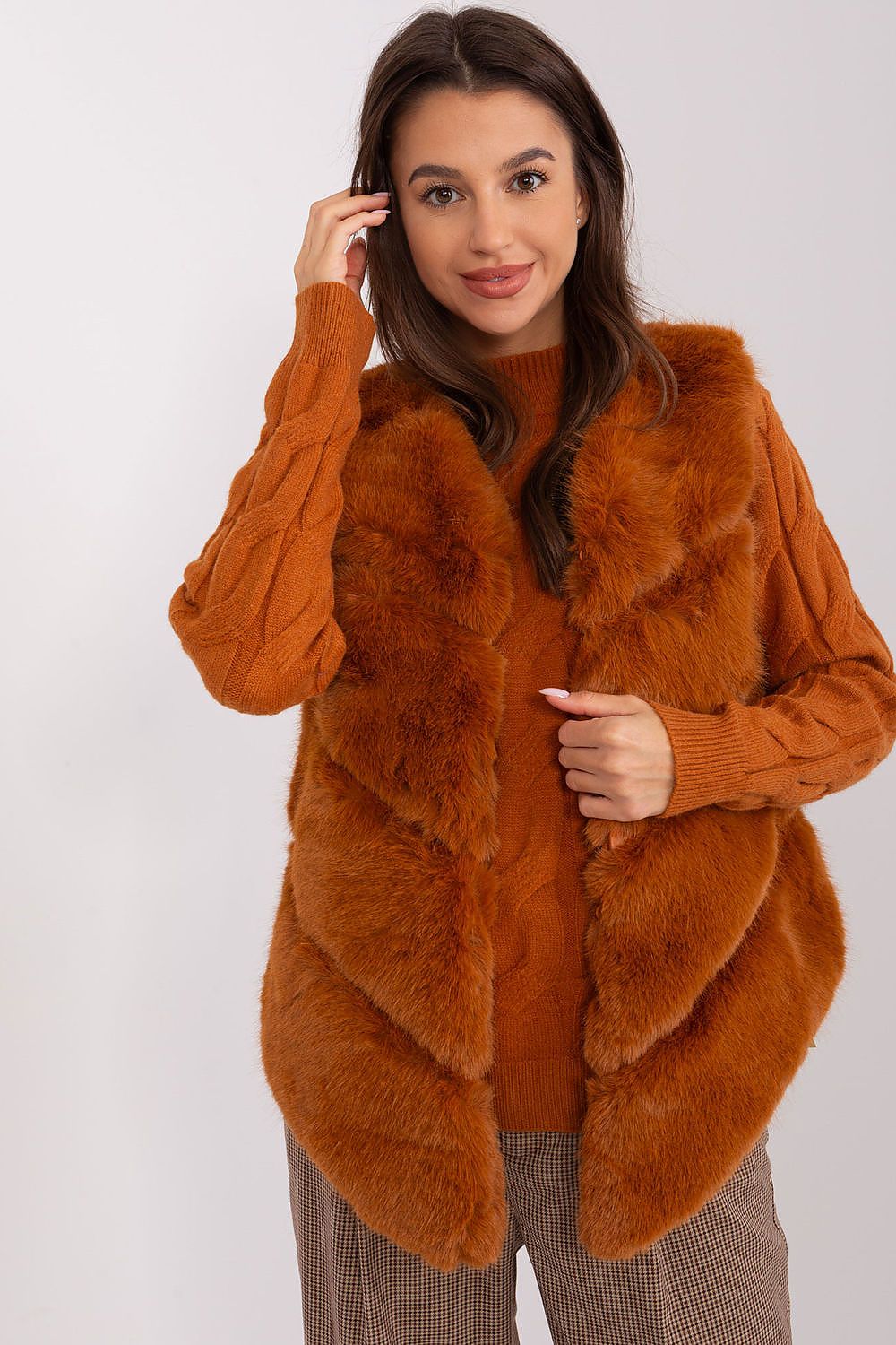Woman wearing a brown fur vest over an orange sweater on a white background