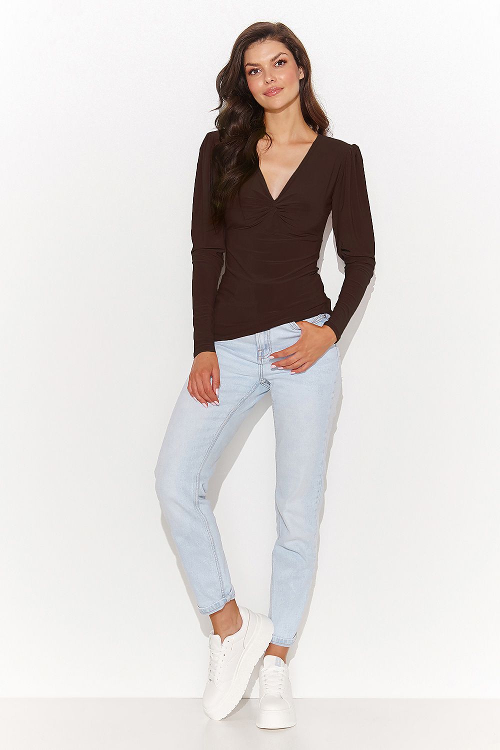 Woman wearing a brown long-sleeve top and light blue jeans on a white background