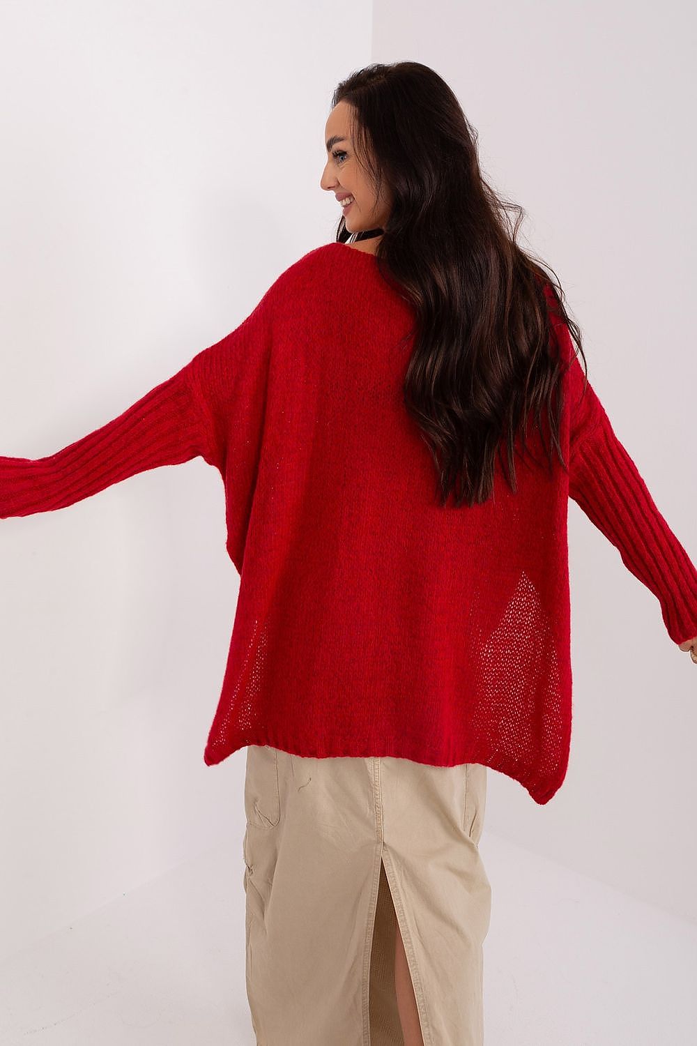 Woman wearing a red sweater with arms outstretched on a white background
